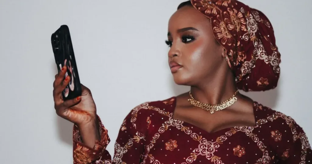Stylish Nigerian woman in traditional attire holding a smartphone