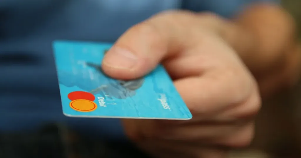 Hand offering a blue debit card for payment, representing everyday spending