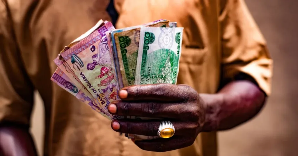 Close-up of a man's hand holding Nigerian naira banknotes outdoors in Bida, Nigeria, representing digital banking and personal finance in Nigeria