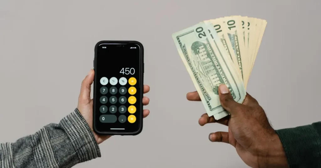 Hands holding cash next to a smartphone calculator, representing budgeting and saving money