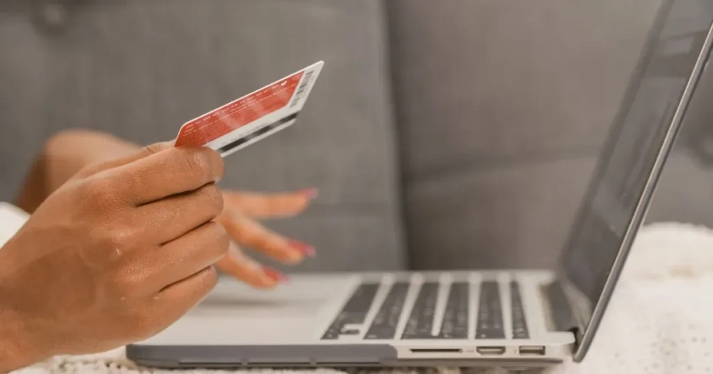 Person holding a bank card while shopping online on a laptop, representing virtual card payments
