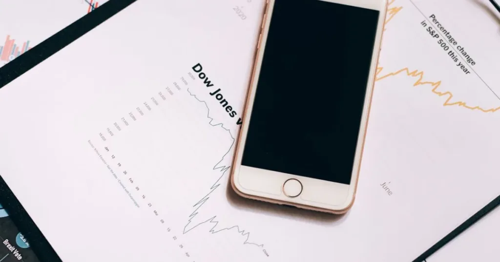 Smartphone resting on financial charts and a clipboard for tracking expenses