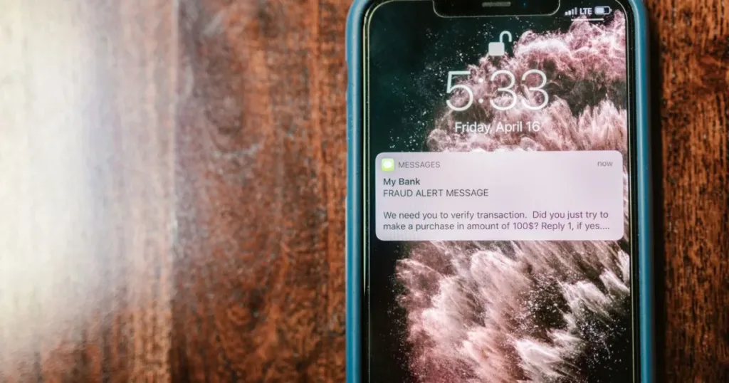 Close-up of a smartphone displaying a fraud alert text message, warning of a fake loan app scam.