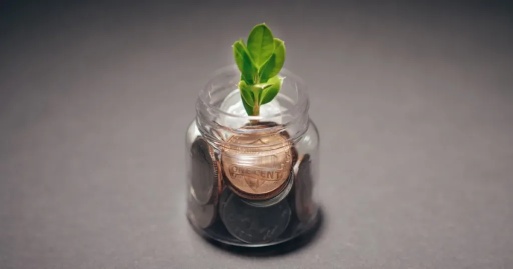 A small green plant growing out of a jar of coins, symbolizing steady improvement of a credit score.