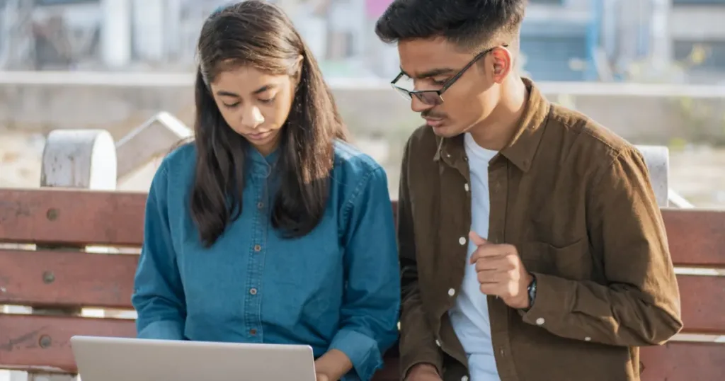 Two young students working together on a laptop, planning their first credit card