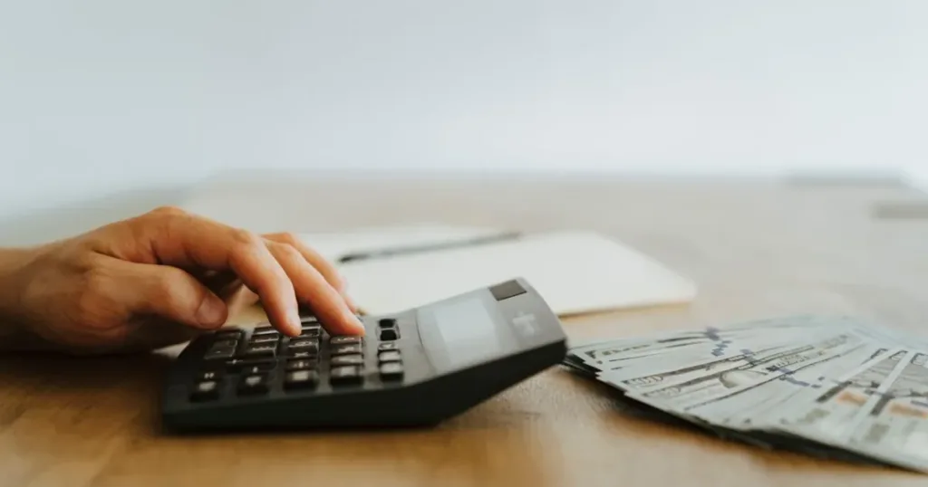 Hand calculating finances with a calculator next to cash