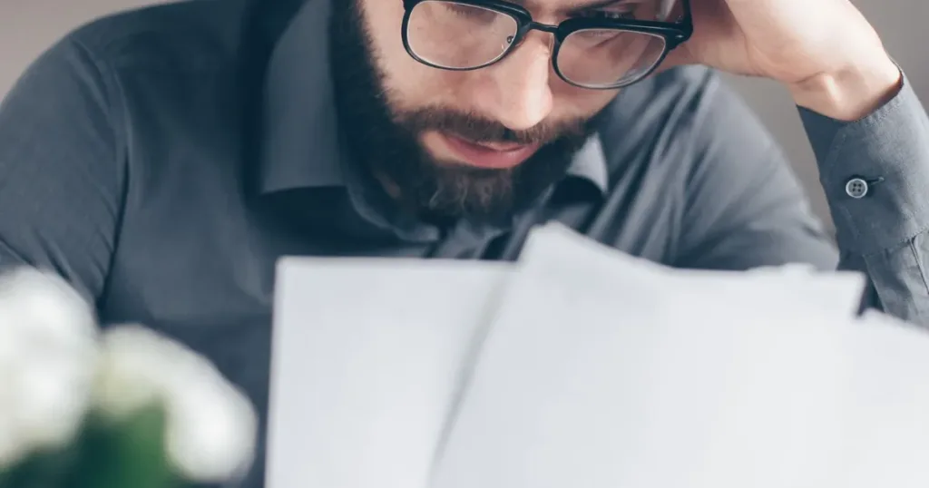 Worried man reviewing financial bills and papers at home