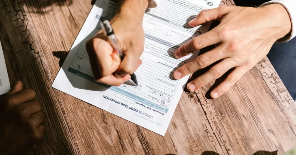 Hands filling out a credit application form with documents on a desk