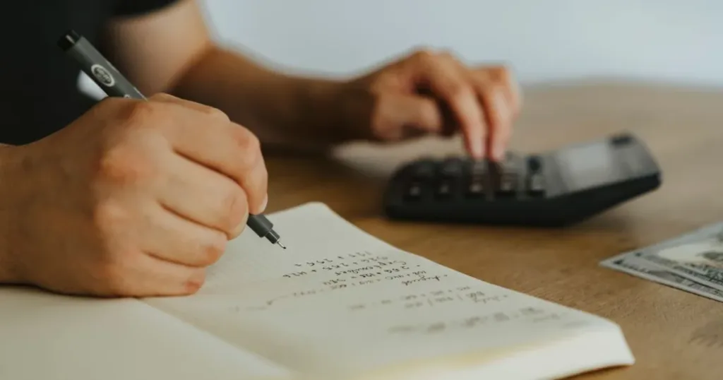 Hands writing calculations in a notebook with a calculator