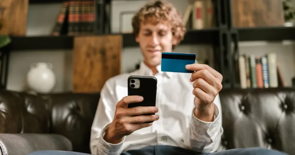 A man smiles while using his smartphone and credit card for an online payment