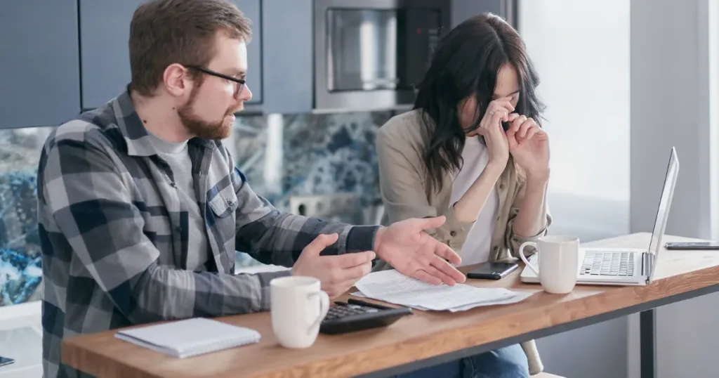 Stressed couple reviewing bills and debts at the kitchen table
