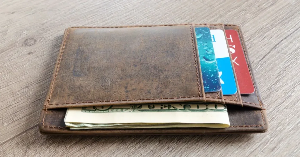 A brown leather wallet with cash and credit cards on a wooden table