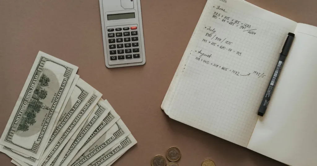 Calculator, notebook and cash on a desk for comparing a credit card and a loan