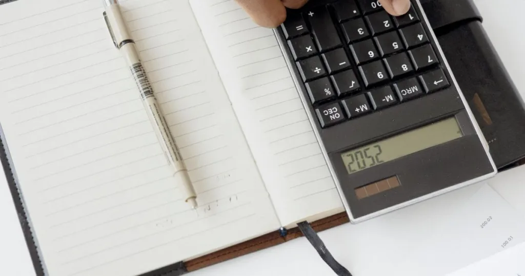 A hand using a calculator with financial documents and notebook