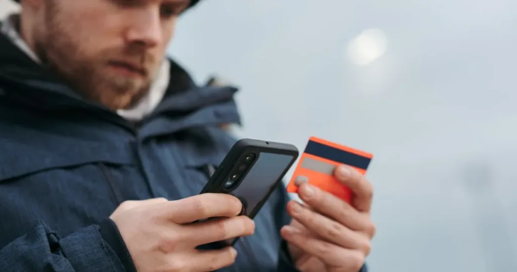 Man entering bank card details on his mobile phone outdoors, comparing banking apps