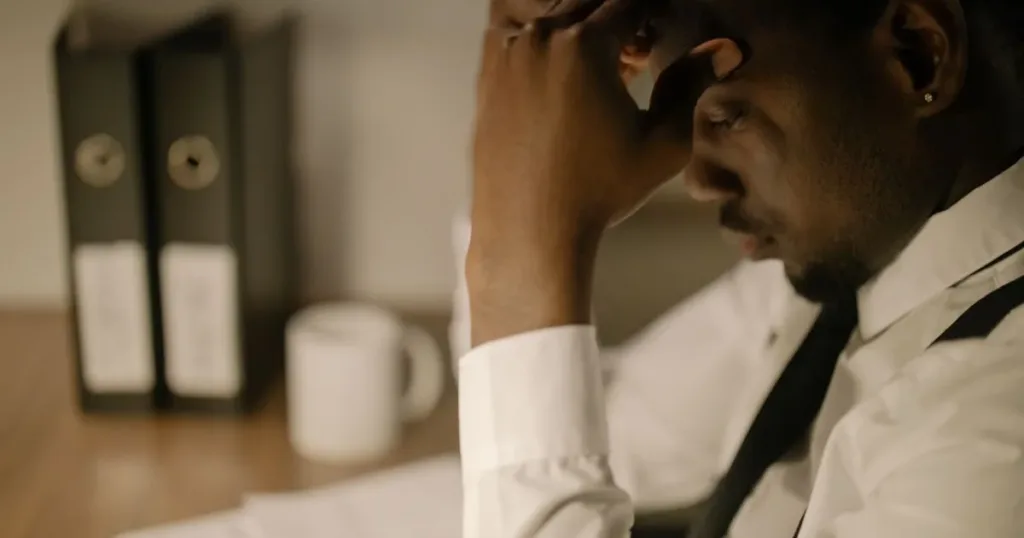Frustrated man holding his head at a desk covered in papers, representing the stress of a rejected loan application.