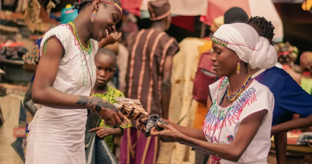 Two Nigerian market women exchanging goods at a busy stall