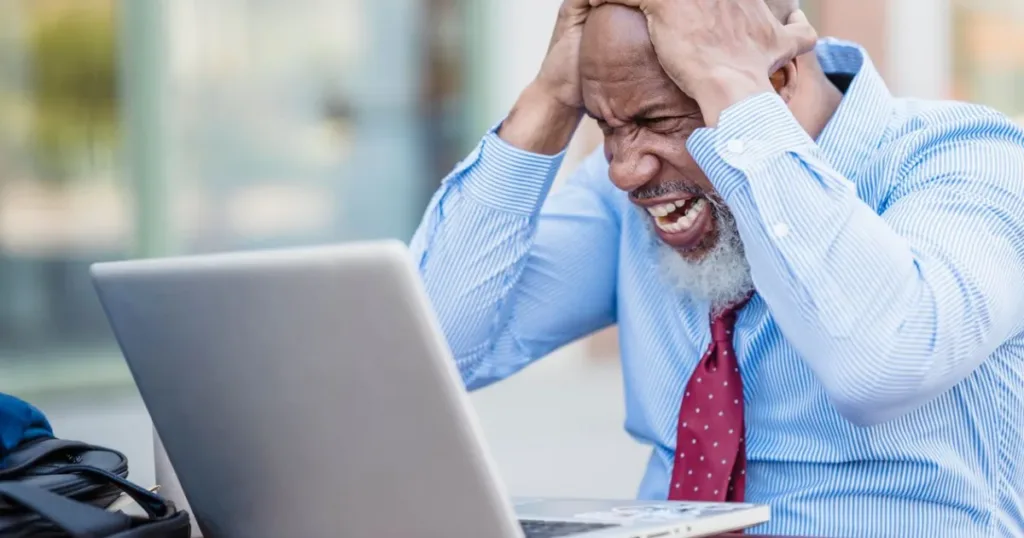 Frustrated man with a laptop outdoors, representing the trap of repeatedly rolling over a loan.