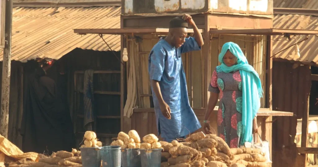 Nigerian market traders selling yams at an outdoor stall, representing small business owners