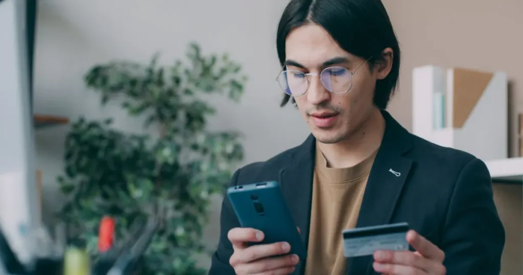 Businessman holding a bank card while using his smartphone for personal banking