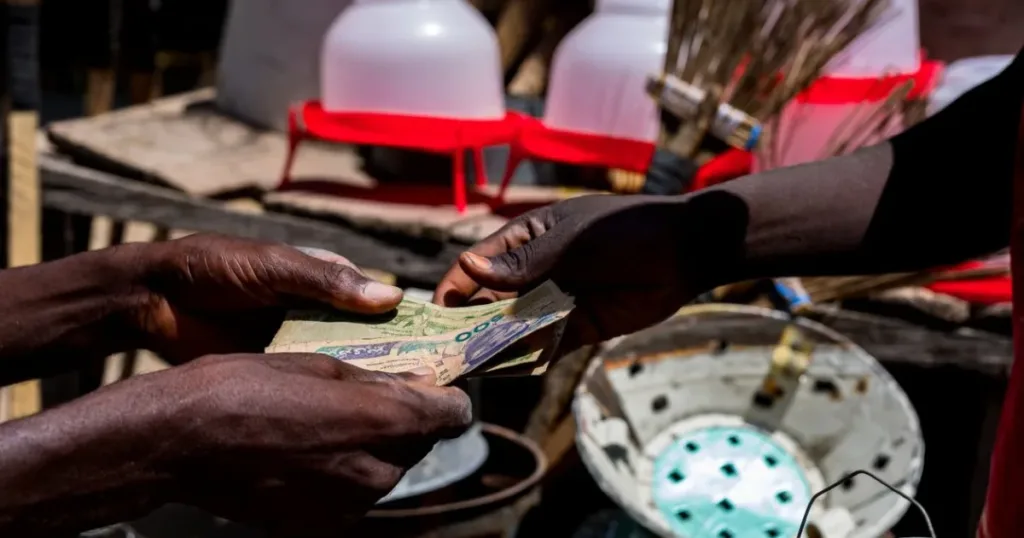 Close-up of hands exchanging Nigerian naira bills at a market, representing a money transfer