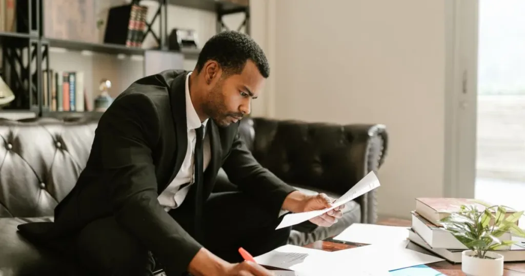 Man in a suit signing documents at a coffee table, representing the decision to pay off old debt before taking a new loan.