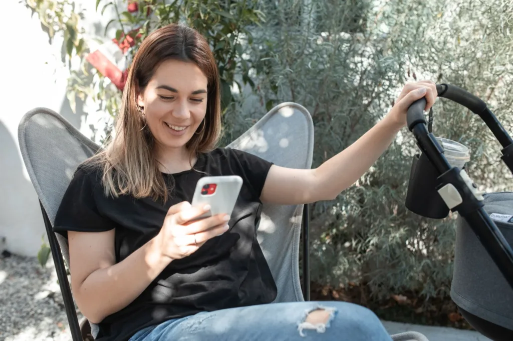 Smiling woman using a smartphone app while sitting outside with a stroller