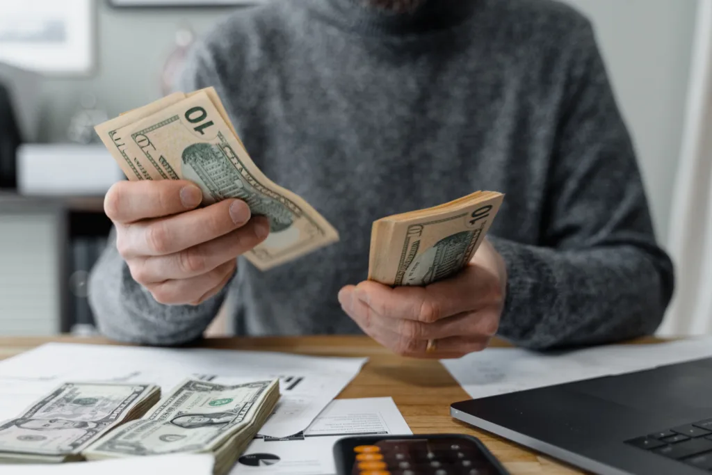 Close-up of a person counting cash with a calculator and paperwork
