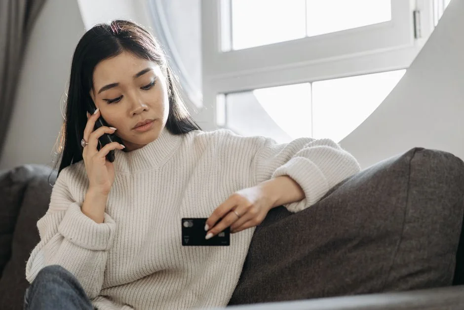 Woman checking her phone and credit card while reviewing her finances at home