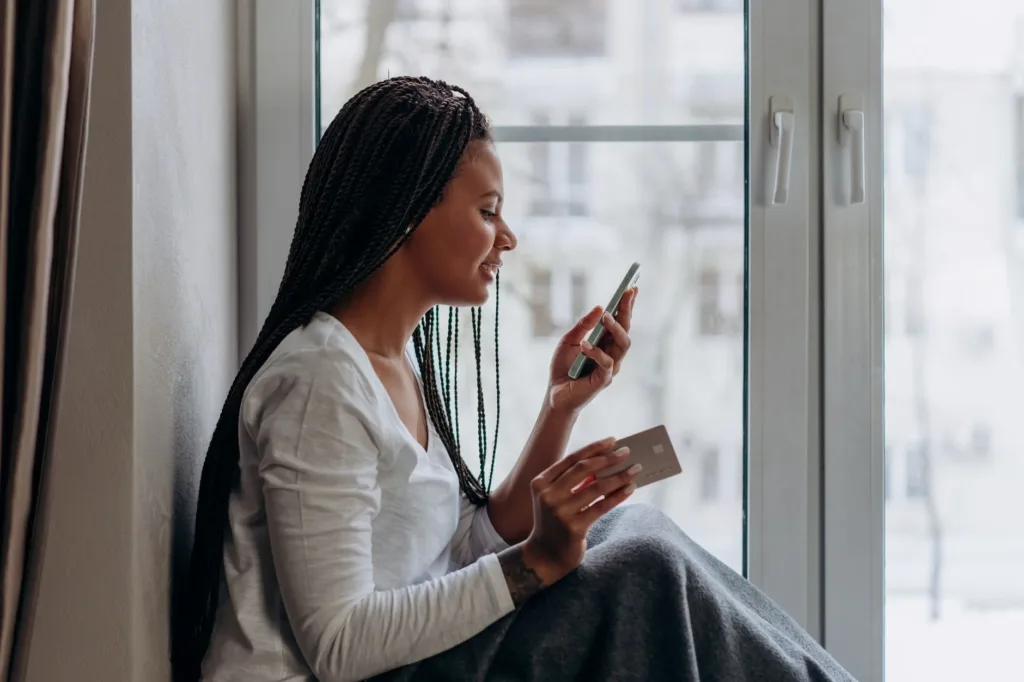 Woman using her phone and holding a card while paying a bill at home
