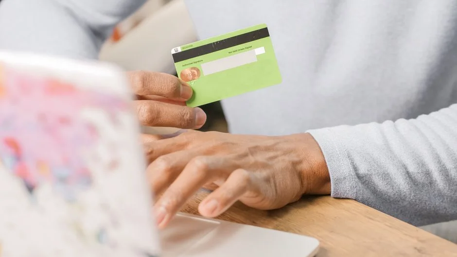 Hands holding a credit card while making an online purchase on a laptop