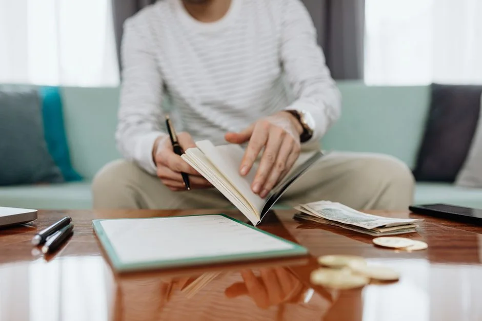 Person reviewing personal finances at a table with a notebook, cash and laptop