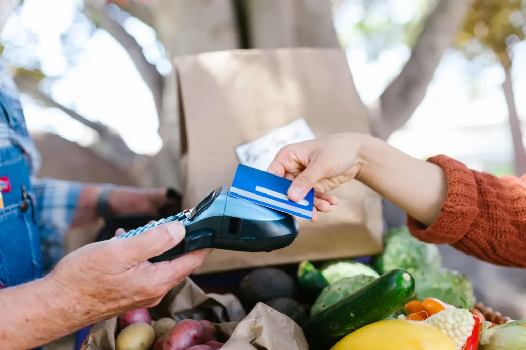 Hand tapping a credit card on a payment terminal while buying groceries
