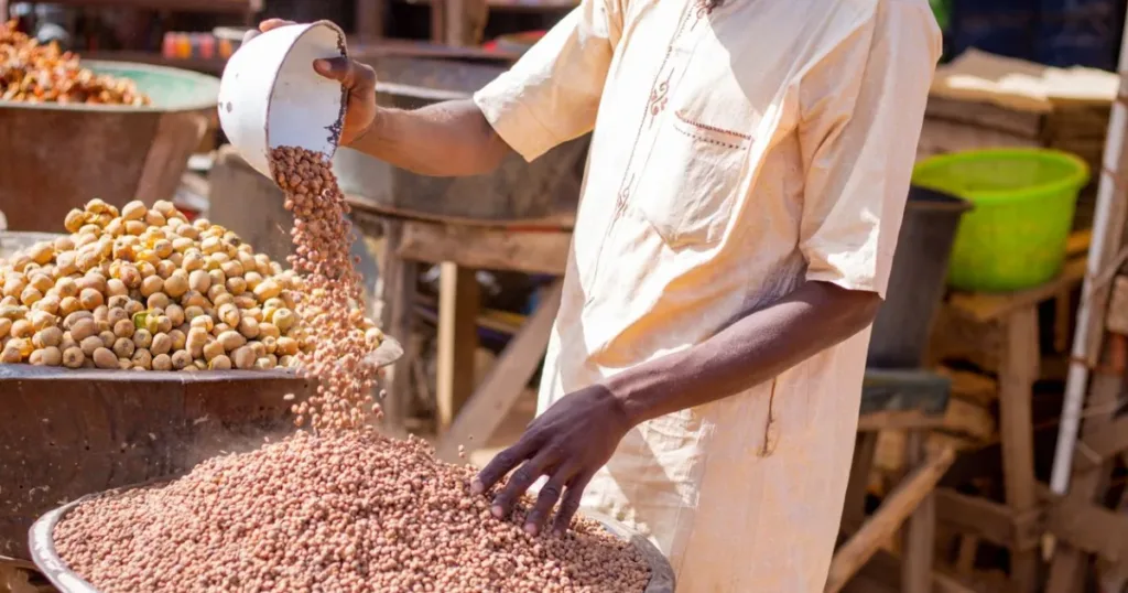 Man pouring and selling grains at a bustling Nigerian market