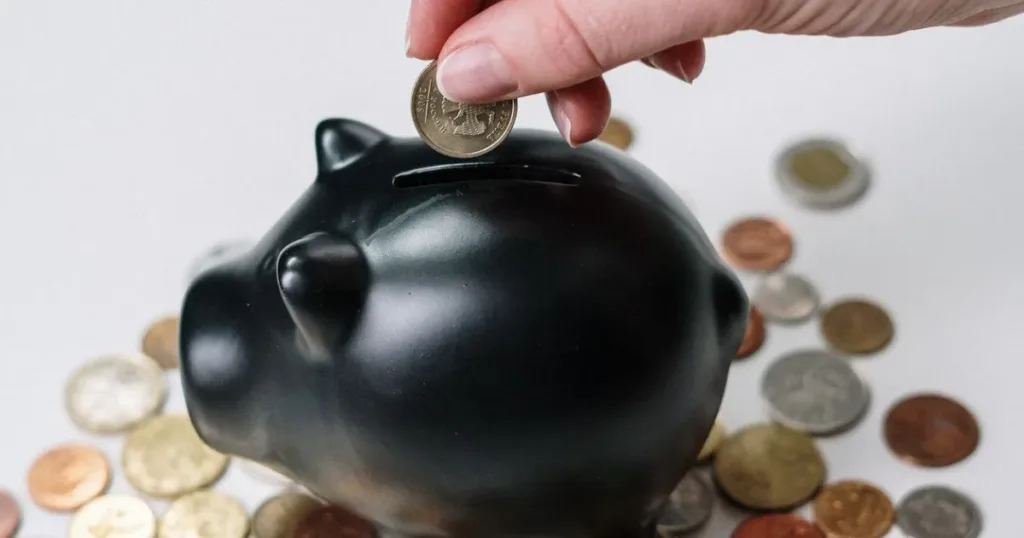 Hand inserting a coin into a piggy bank to save for rent in Lagos or Abuja