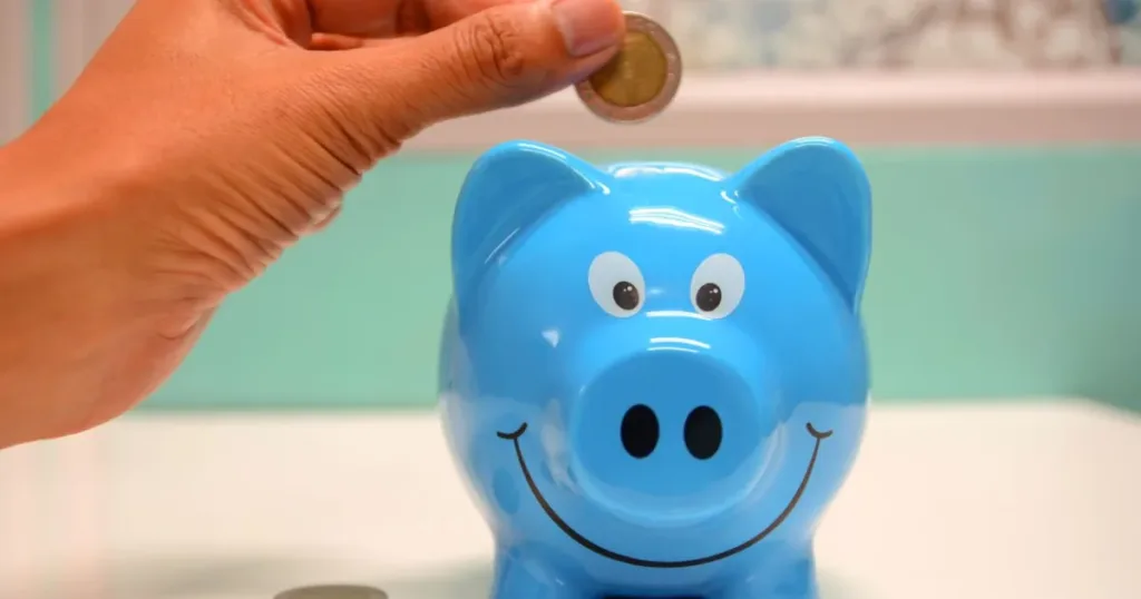 Hand dropping a coin into a piggy bank, representing savings apps for salary earners