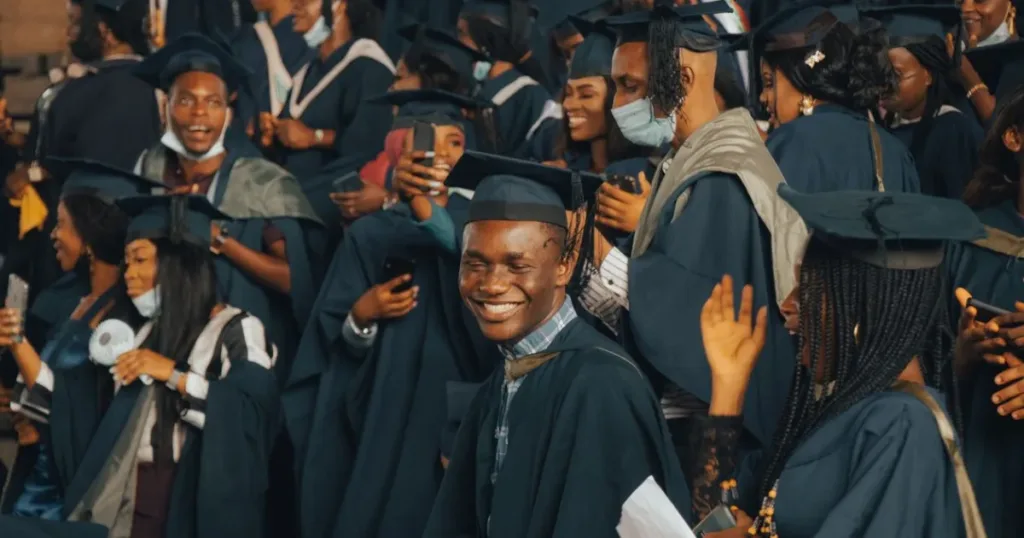 A joyful crowd of graduates in colorful academic regalia celebrating at a Nigerian university ceremony