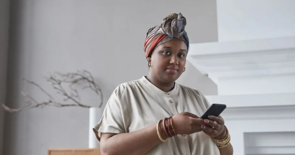 A confident woman using a smartphone indoors, representing mobile money and digital wallet apps