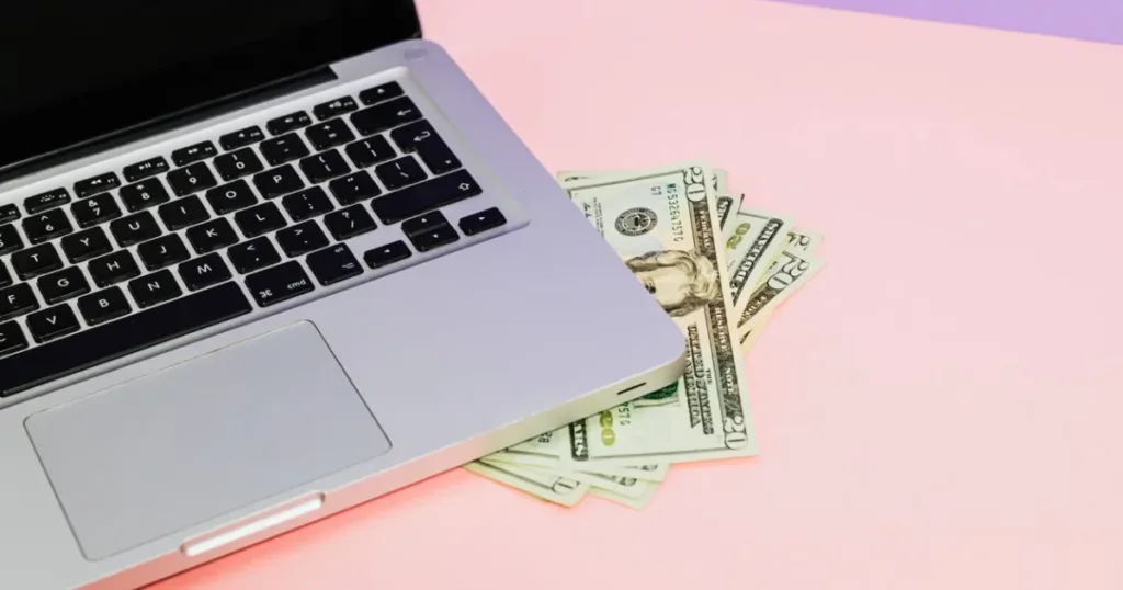 A laptop with US dollar bills resting on top of it, symbolizing foreign currency and online finance