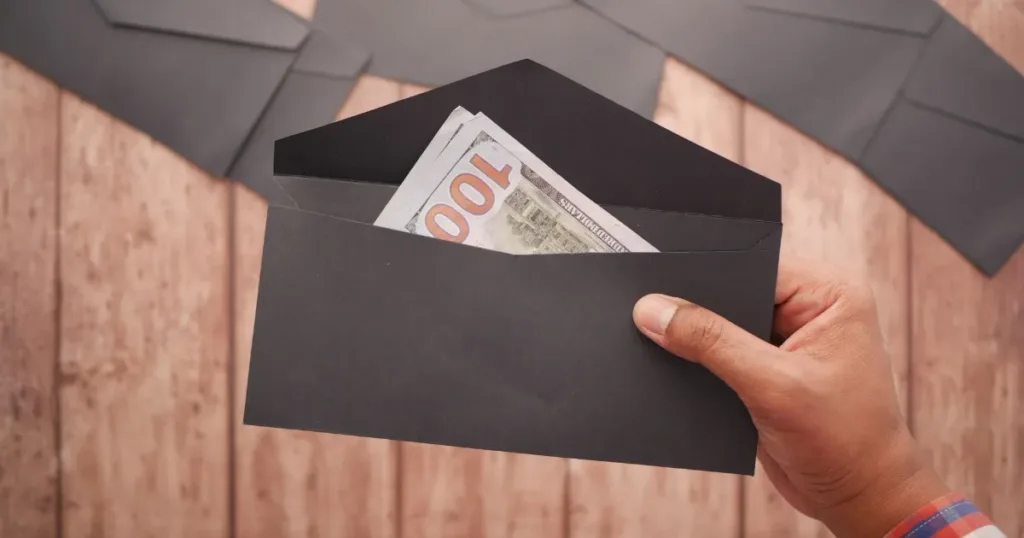 Hand holding a black envelope with a cash bill on a wooden surface