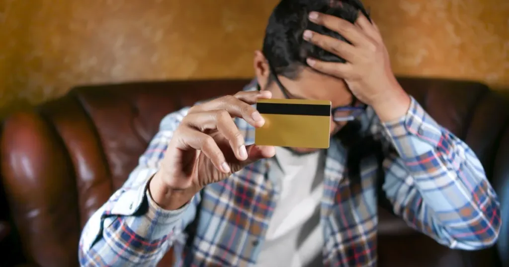 Person looking stressed while holding a credit card, representing the minimum payment trap