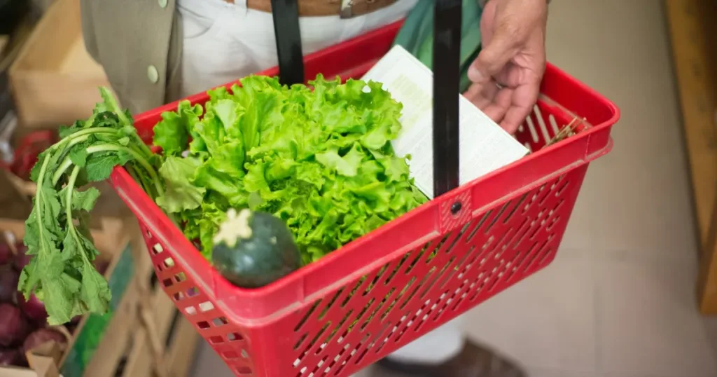 Close-up of a hand carrying a shopping basket full of fresh greens in a market