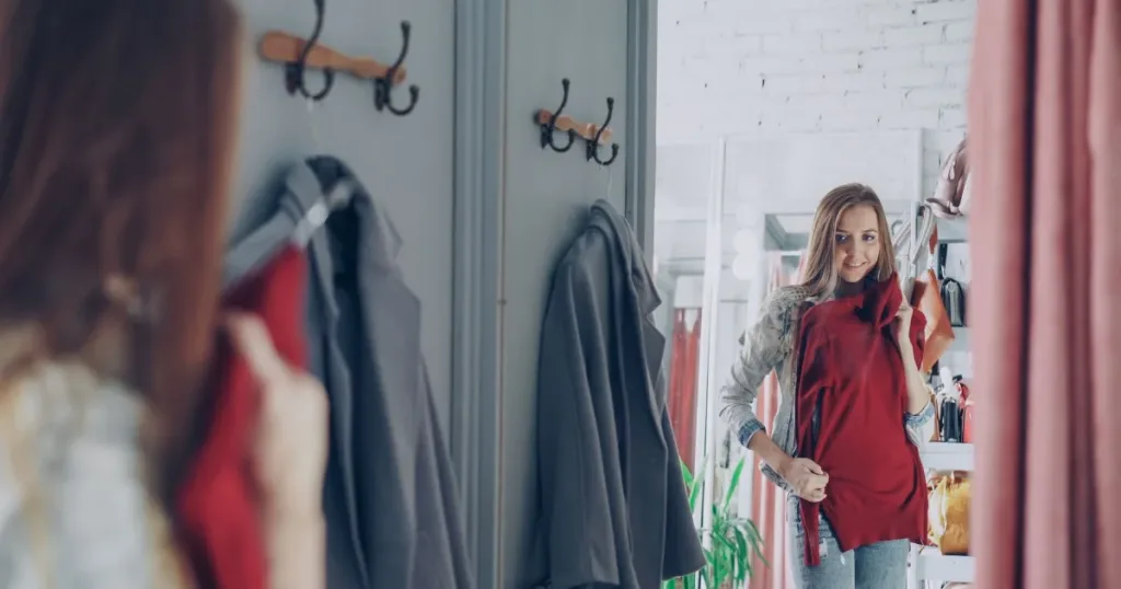 Smiling woman in a fashion boutique fitting room holding a red dress